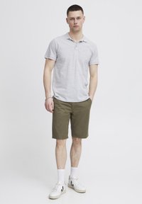 Männer Polohemd in Grau aus Baumwolle, kombiniert mit olivgrünen Shorts. Die Schuhe sind weiße Sneakers und weiße Socken. Schlichtes Design.