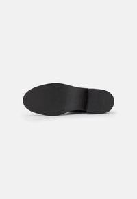 Semelle de chaussure synthétique noire avec une texture lisse, un bout arrondi, un talon effilé et un motif de semelle minimal pour une meilleure adhérence.