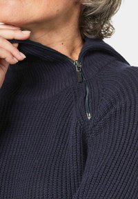 Navy Zip-Jacke aus geripptem Material mit hohem Kragen und schwarzem Reißverschluss. Die Textur wirkt weich und gestrickt.