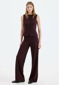 Vestă burdeos croită cu decolteu rotund și nasturi în față, asortată cu pantaloni largi de aceeași nuanță. Material neted, cu textură minimă.