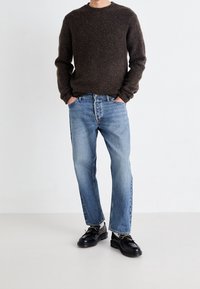 Pull en laine marron, jean droit bleu clair, et chaussures en cuir noires. Le pull a un col rond et des poignets côtelés.