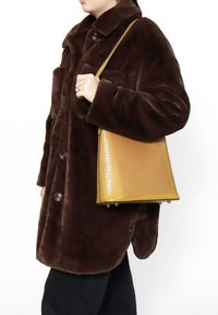 Cappotto in pelliccia sintetica marrone con grandi bottoni, abbinato a una borsa gialla testurizzata con forma strutturata e piedi metallici.