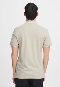 Beige polo-shirt med korte ærmer, blød tekstur, diskret krave og kontrasterende kanter på ærmerne. Ingen synlige logoer eller mønstre.