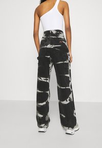 Pantalones vaqueros de pierna ancha negros con un patrón de tie-dye en gris y blanco, que presentan dos bolsillos traseros y bolsillos laterales tipo cargo. Textura de denim suave.