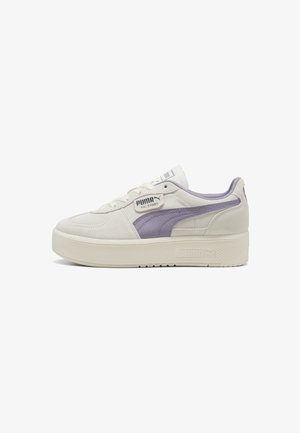 Bílé semišové tenisky s lila pruhem PUMA, šněrovací design, plochá podrážka, texturovaná platforma a logová nášivka na boku.