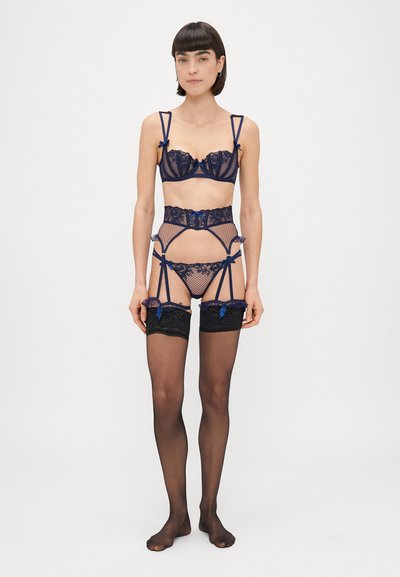 Tumed alusseelised pesu komplekt, mis sisaldab traadiga rinnaalust, sukapaela ja sobivaid sukkpükse. Omab lipsukesi ja poolläbipaistvaid detaile koos keerukate elementidega.