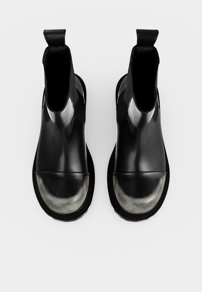 Paire de bottines en cuir noir avec embouts métalliques ronds et languettes sur fond blanc.