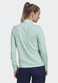 Hellgrünes langärmliges Oberteil mit hohem Kragen, glatter Textur, tailliertem Design und Daumenöffnungen an den Bündchen, kombiniert mit navyfarbigen Hosen.