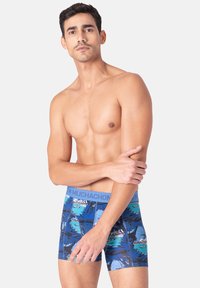 Siniset boxerit trooppisella kuviolla, jossa on vaaleansiniset vyötärönauhat, joissa lukee "MUCHACHON." Valmistettu pehmeästä, joustavasta materiaalista.