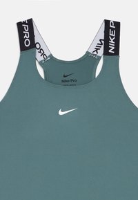 Τιρκουάζ αθλητική μπλούζα Nike Pro με εφαρμογή, με λευκό λογότυπο Nike μπροστά και ελαστικές τιράντες με μαύρο και άσπρο branding.