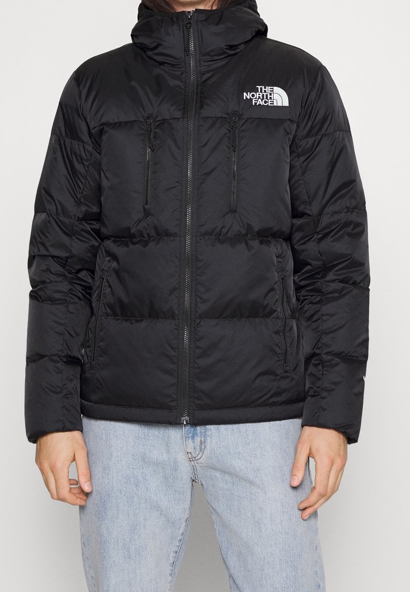 Chaqueta de plumas negra con capucha, que cuenta con bolsillos en el pecho con cierre, puños acanalados y el logotipo de The North Face en el hombro izquierdo.