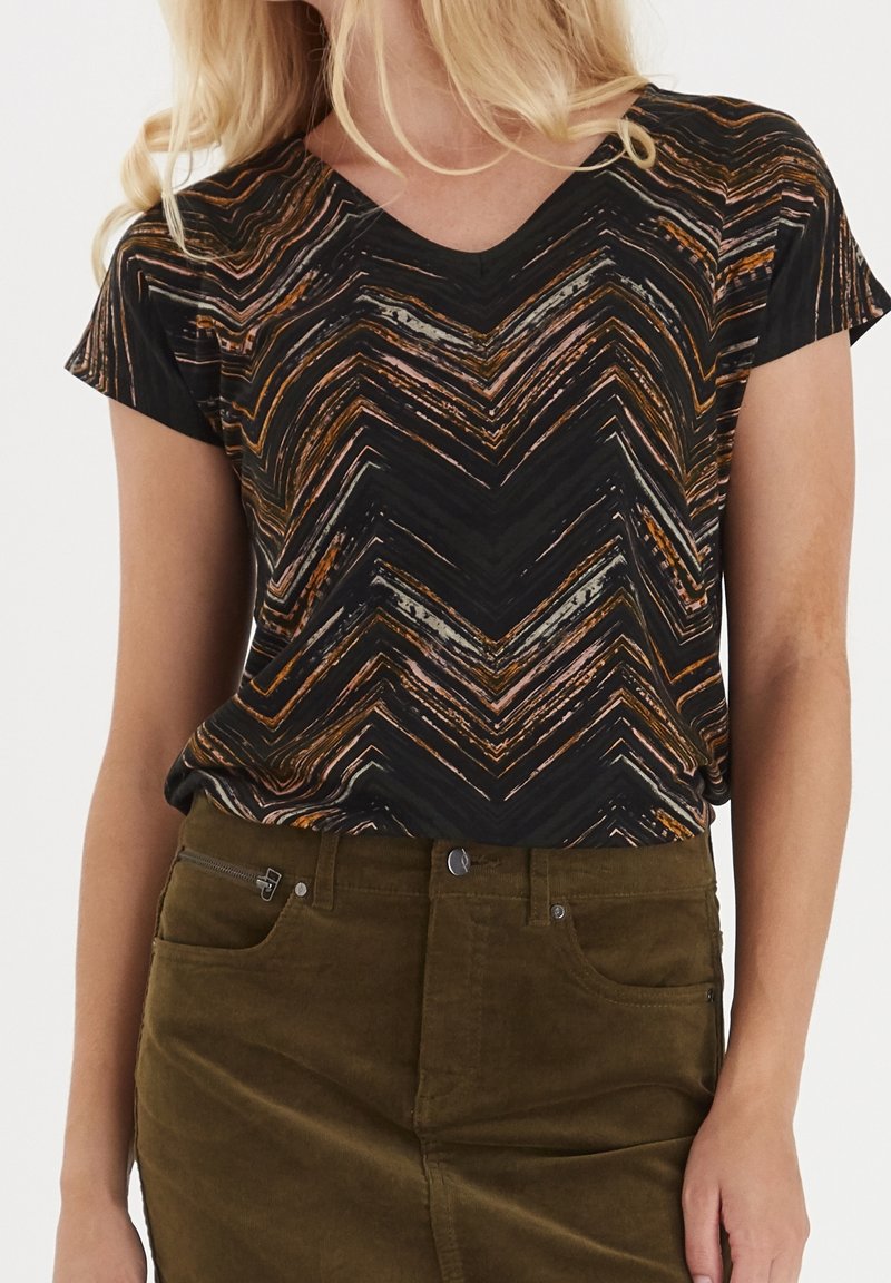 Černé a oranžové tričko s krátkým rukávem a vzorem ve tvaru chevronu s výstřihem do V, spárované s olivově zelenou manšestrovou sukní s postranní kapsou na zip.