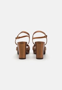 Brown metallic platform heels with a braided strap design, adjustable ankle buckle, and sturdy block heels. Smooth texture throughout.