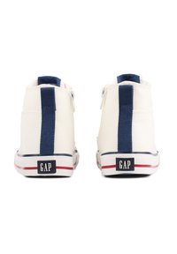 Witte canvas hoge sneakers met een marineblauwe streep, witte rits, rode en marineblauwe zool en 'GAP' logo op de hiel.