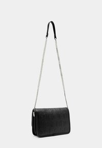 Bolso cruzado de cuero negro con diseño de logo en relieve, cuenta con una correa de cadena y una solapa negra lisa. Textura suave, forma rectangular.
