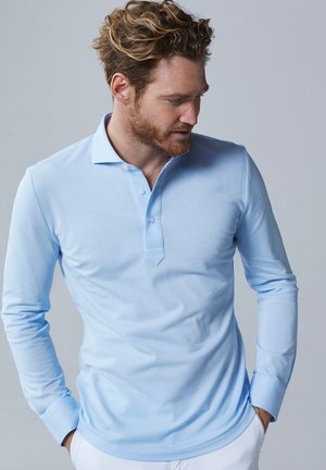Lichtblauwe polo met lange mouwen, voorzien van een twee-knopen sluiting, zacht materiaal, slanke fit en vlakke kraag. Casual gedragen door een man.