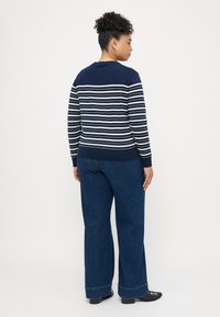 Ναυτικό ριγέ πουλόβερ με λευκές γραμμές, στρογγυλή λαιμόκοψη και ριμπ μανσέτες, σε συνδυασμό με φαρδιά τζιν παντελόνια και μαύρα παπούτσια.