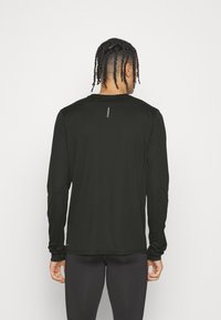 Långärmad svart träningsskjorta i lätt, slät tyg. Har en rundad halsringning och en liten logotyp tryckt på övre ryggen.