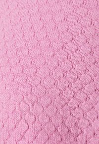 Gros plan sur un tissu tricoté rose avec un motif texturé présentant de petits trous répartis uniformément sur la surface.