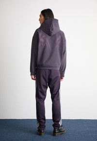 Dark gray hoodie with a textured pink design on the back, paired with matching sweatpants featuring white side stripes and black shoes.