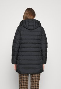 Svart puffjacka med huva, med horisontell sömnad och medellång längd, i kombination med byxor i brun hundtandsmönster.