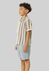 Chemise à manches courtes avec un motif zigzag bleu et crème, design avec col, associée à un short bleu clair, le tissu a un fini texturé.