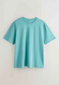 T-shirt turquoise uni à manches courtes et col rond suspendu sur un fond gris clair.