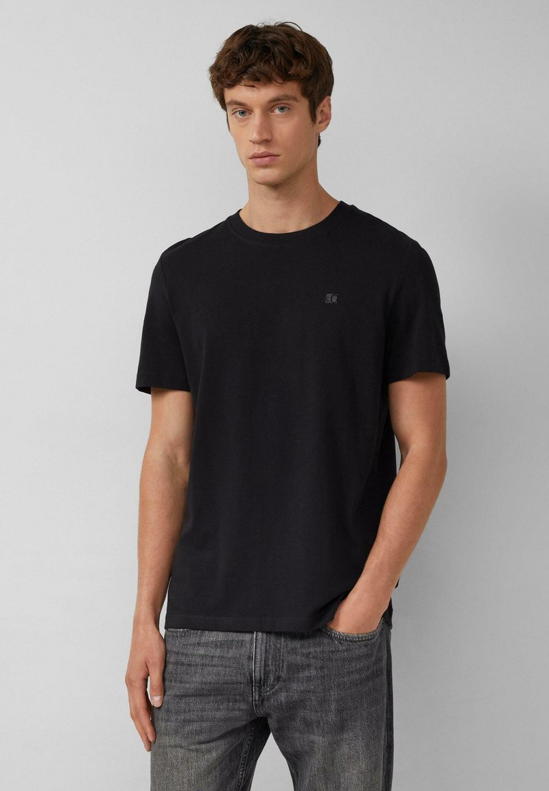 Zwarte t-shirt met korte mouwen van lichtgewicht katoen, voorzien van een ronde halslijn en een klein logo in een subtiele tint, gecombineerd met grijze jeans.