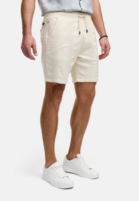 Helle shorts mit einer strukturierten Optik, mit Seitentaschen und einem Kordelzugbund. Kombiniert mit weißen Turnschuhen.