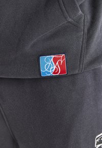 Donkergrijze stof met een klein rechthoekig stuk dat blauwe en rode secties laat zien en ingewikkelde witte schriftletters.