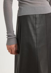 Maglietta grigia a maniche lunghe con costine abbinata a una gonna di pelle nera, caratterizzata da una texture liscia e cuciture verticali per un tocco di dettaglio.
