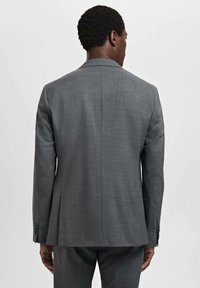 Veste de costume grise sur mesure au design épuré, avec des revers crantés et un dos structuré. Fabriquée à partir d'un tissu texturé avec un léger éclat.