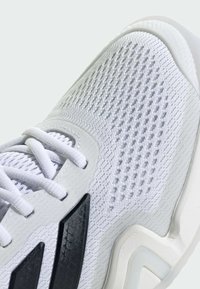 Biele športové topánky s textúrovaným vrchom, sieťovinovým vzorom, čiernymi akcentmi a dizajnom tlmiacej podrážky. Šnúrky sú integrované do štruktúry.