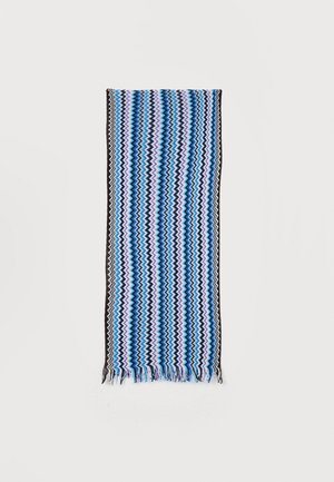 Sciarpa lunga e rettangolare con strisce a zigzag in blu, nero, viola e bianco, bordi frangiati, distesa su uno sfondo bianco.
