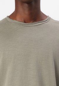 Olivenfarbene T-Shirt mit rundem Ausschnitt, mit einem Rohkantensaum und weichem, strukturiertem Stoff. Das Design ist schlicht und klassisch.