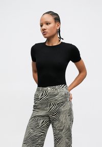 Top negro de manga corta con textura acanalada, combinado con pantalones de talle alto que presentan un patrón de rayas de cebra en negro y crema. Tela suave, ajuste estilizado.