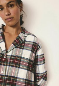 Plaid marškiniai su mygtukais, vaizduojantys raudonų, žalių ir mėlynų juostų mišinį, baltas pagrindas, kontrastingas apykaklė ir kairėje krūtinės pusėje kišenė.