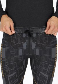 Schwarze Sporthose mit einem geometrischen grauen Muster, ausgestattet mit einem Kordelzugbund und zwei schrägen Taschen vorne, beschriftet mit "SWEDEMOUNT."