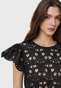 Black top with intricate cut-out floral patterns, short ruffled sleeves, and a round neckline. Textured fabric with open sections.
