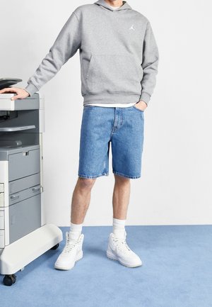 Sudadera gris con bolsillo canguro, pantalones cortos de mezclilla y zapatillas altas blancas sobre una alfombra azul al lado de una impresora / fotocopiadora en monochrome.