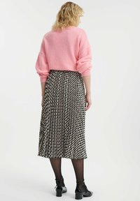 Różowy sweter z dzianiny z opadającymi ramionami w połączeniu z czarną i kremową spódnicą w plisowany wzór. Całość uzupełniają czarne buty na kostkę.