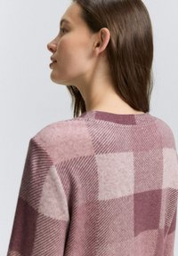 Maglione con un motivo a scacchi in tonalità di rosa, con una texture morbida e scollatura a girocollo, mostrato da un'angolazione laterale.