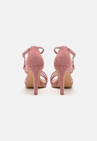 Sandales à talons hauts en daim rose avec des brides de cheville, design à bout ouvert et accents en cristal décoratifs sur les brides.