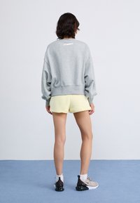 Sweatshirt gris avec des épaules tombantes, un short jaune clair et des baskets beiges. Tissus doux avec une coupe décontractée, minimalisme des détails de marque.
