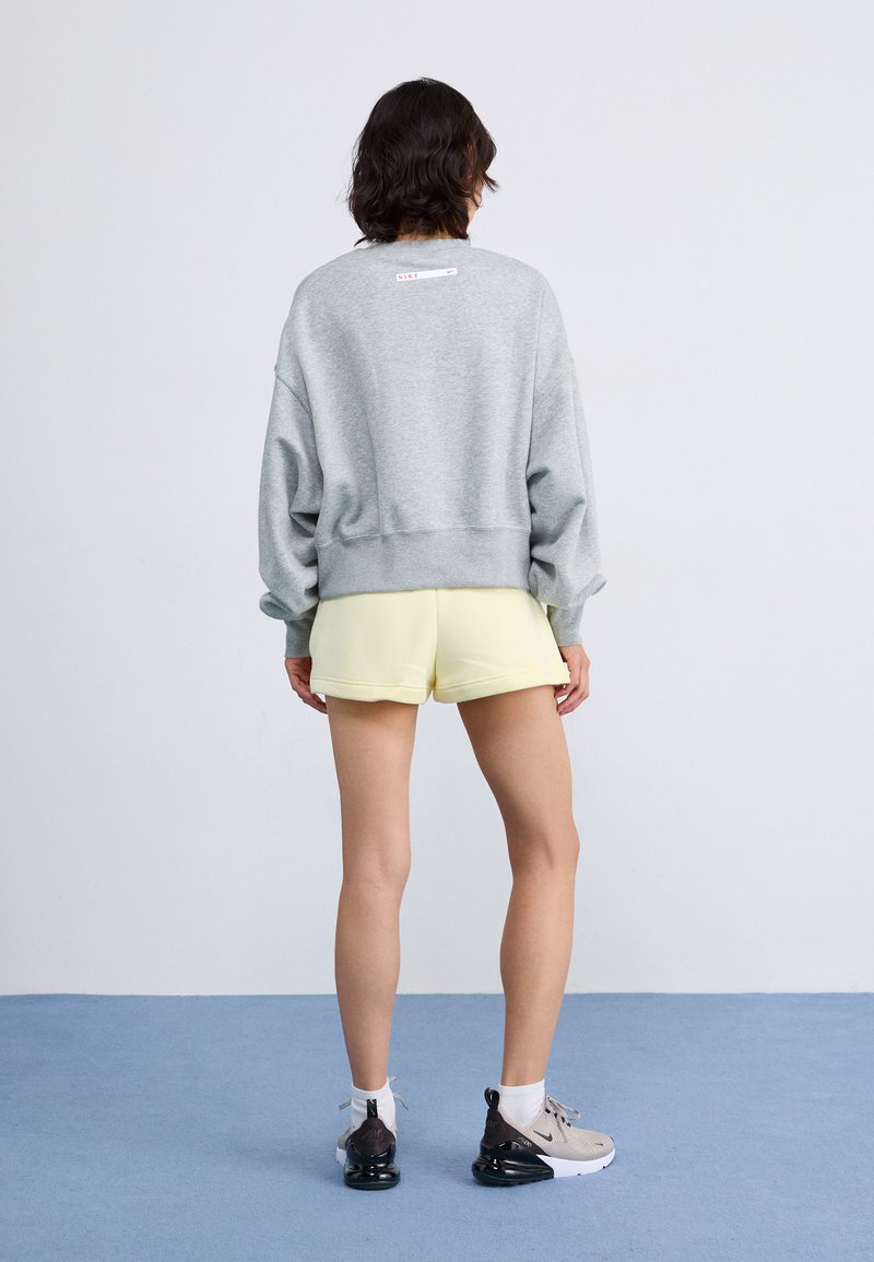 Sudadera gris con hombros caídos, un par de pantalones cortos ligeros amarillos y zapatillas beige. Tejidos suaves con un corte relajado, detalle de marca mínimo.