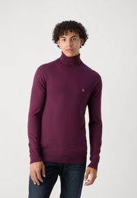 Pull à col roulé à manches longues en violet foncé, fait d'un matériau doux. Il présente un petit logo brodé sur la poitrine et des poignets côtelés.