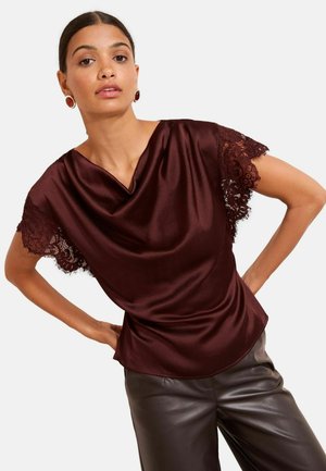 Burgundy satinblus med spetskortärmar, draperad halsringning och slät textur, kombinerad med svarta läderbyxor.