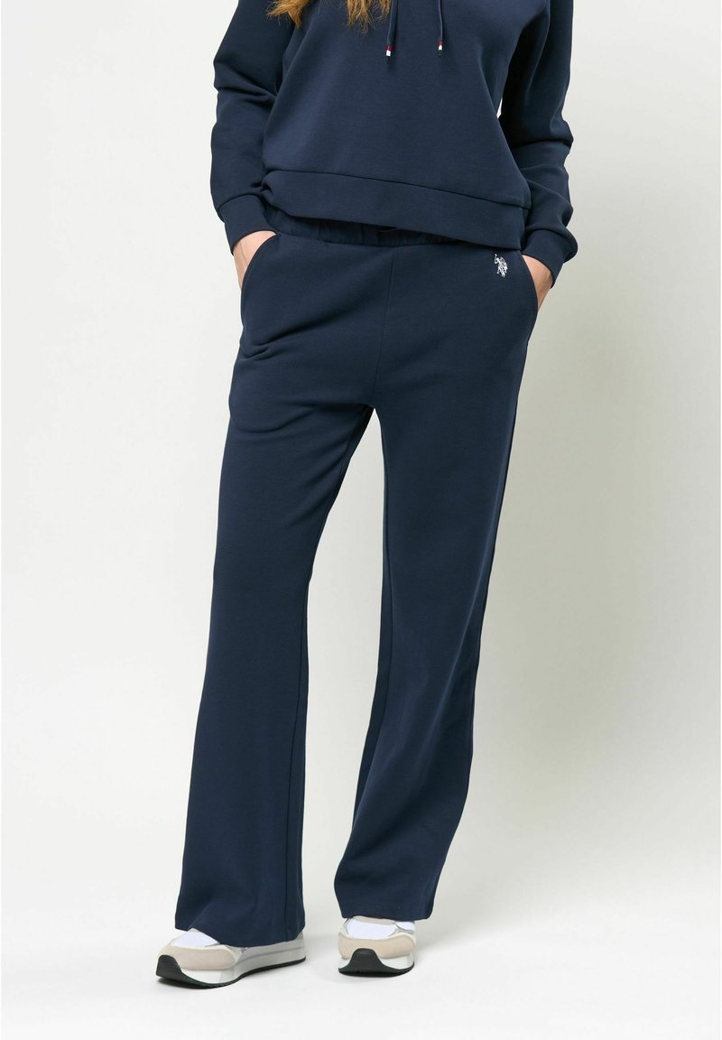 Navy krāsas sporta bikses atvieglotā piegriezumā, izgatavotas no mīksta auduma, ar sānu kabatām un izšūtu logotipa detaļu. Apvienotas ar atbilstošu jaku.
