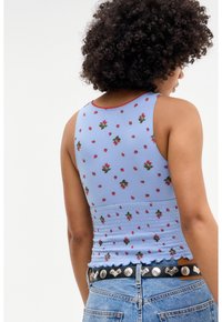 Blå linne med blommigt jordgubbstryck, med en smockdesign, vågig nederkant och röda detaljer, som matchas med högmidjade jeans.