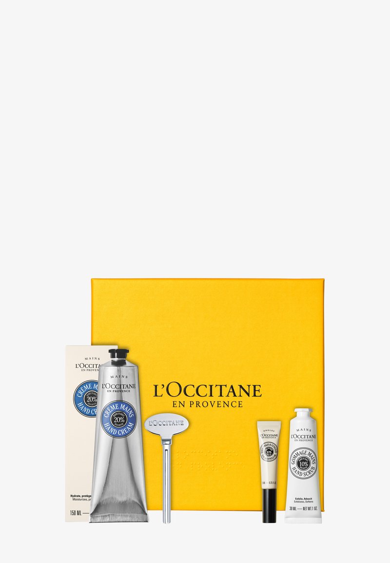 Ensemble de soins pour les mains L'Occitane comprenant une crème pour les mains, un gommage pour les mains, un baume à lèvres, une clé en métal, le tout placé devant une boîte jaune avec le nom de la marque.